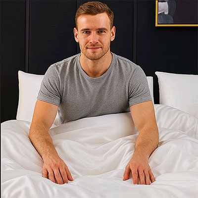 homme assis dans lit souriant avec housse de couette blanche