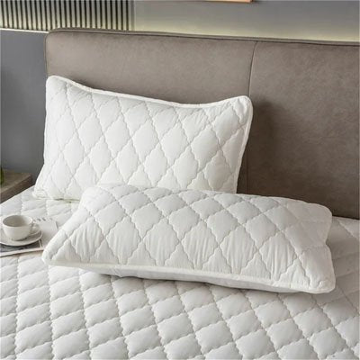protege oreiller matelassée blanche disposé sur lit