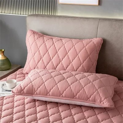 protege oreiller matelassée rose disposé sur lit